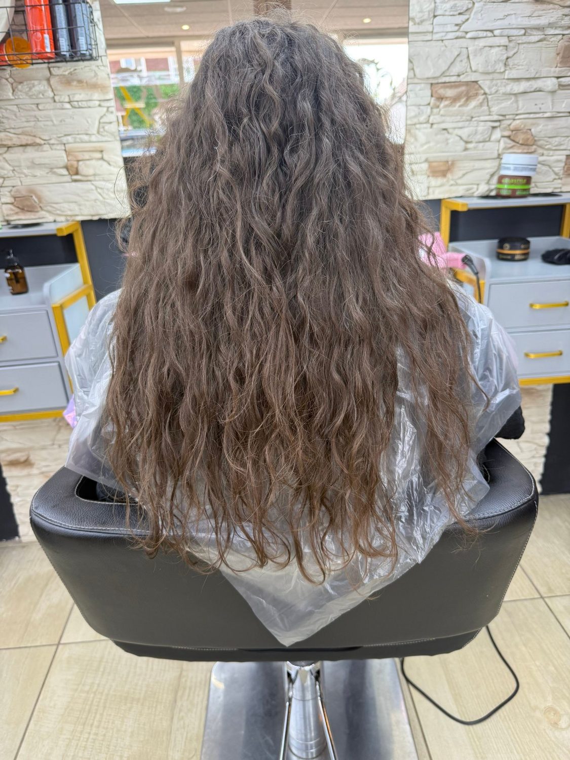 Lang bruin haar met natuurlijke golven, in de stoel voor de spiegel